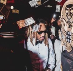 a man with dreadlocks standing in front of money falling from his head at a party