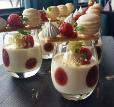 several desserts are arranged in small glasses on a table with strawberries and whipped cream