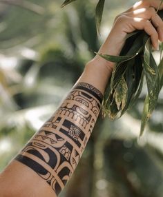 a person's arm with tattoos on it holding onto a tree branch in front of some leaves