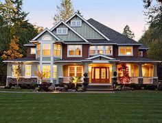 a large house with lots of windows and lights on it's front porch in the evening