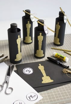 some black and gold paper bottles are sitting on a table next to scissors, markers, pens and other items