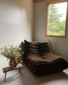 a brown futon sofa sitting in front of a window next to a small table with flowers