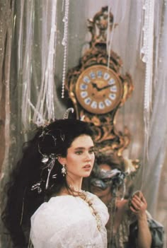 a woman in a white dress standing next to a clock