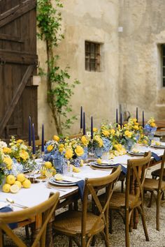 a long table is set with yellow and blue floral centerpieces for an outdoor dinner