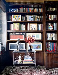 a bookshelf filled with lots of books next to a vase and statue on top of a table