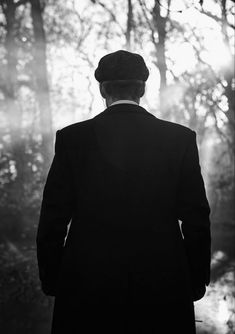 a man in a suit and hat looking out into the woods