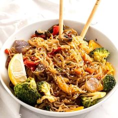 a white bowl filled with noodles, broccoli and lemon wedged chopsticks