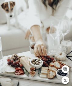 a woman is preparing food on a tray with cheese, crackers, and grapes