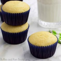 three blue and yellow cupcakes sitting on a table next to a glass of milk