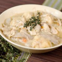 a white bowl filled with chicken and dumplings on top of a wooden table next to a sign