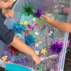 two young children are playing with glitter and star decorations in a plastic bin filled with confetti