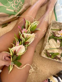 a person laying on the ground with flowers in their lap and feet covered by sand