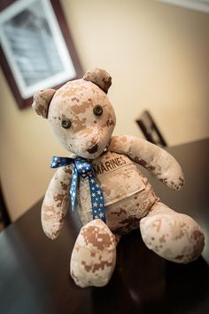 a teddy bear that is sitting on top of a table with a blue ribbon around it's neck