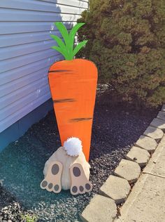 a fake carrot and two feet are on the ground next to a house with blue siding