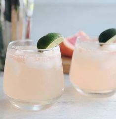 two glasses filled with drinks sitting on top of a table next to grapefruits