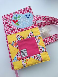 a pink and yellow patchwork book with a tag on it's cover sitting on a table