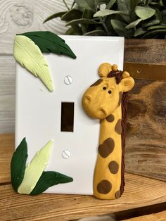 a giraffe head is mounted to the side of a light switch cover with leaves on it