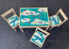 three children's wooden chairs and table with clouds painted on the top, sitting on a carpeted floor