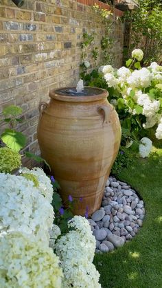 a large vase sitting on top of a grass covered ground next to flowers and bushes