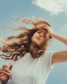 a woman with her hair blowing in the wind, looking up at the blue sky