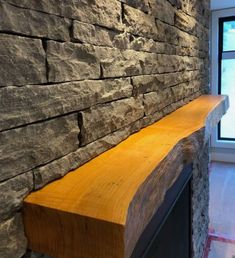 a wooden shelf sitting next to a window in a room with stone walls and flooring