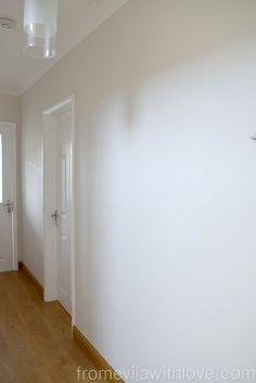 an empty room with white walls and wood flooring in the foreground is a door to another room