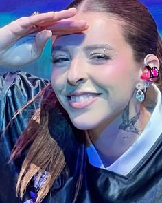 a woman with piercings on her ears smiles at the camera while she holds her hand up to her head