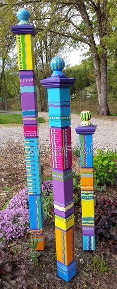 three tall colorful wooden poles in the middle of a garden