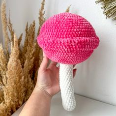 a hand holding a pink and white knitted object in front of some dried plants