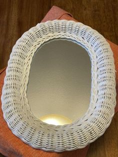 a white wicker mirror sitting on top of a wooden table next to an orange napkin