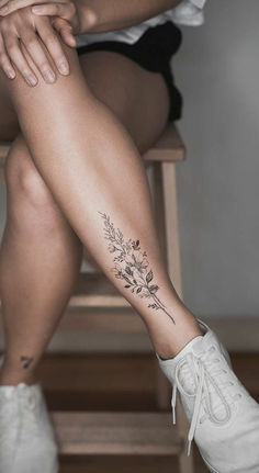 a woman sitting on a chair with her legs crossed and flowers tattooed on the leg