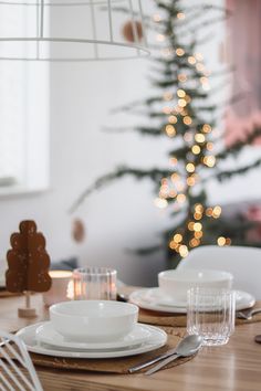 a table set with plates and silverware in front of a christmas tree decorated with lights