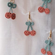 three crocheted cherries hanging from hooks on a white cloth covered tablecloth