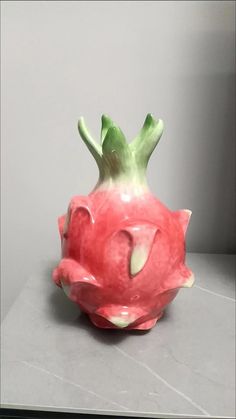 a pink and green vase sitting on top of a gray counter next to a white wall