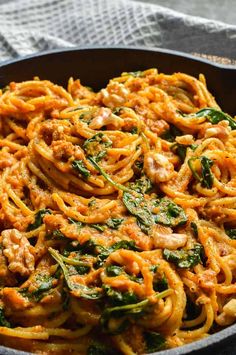 a skillet filled with pasta and spinach on top of a table next to a towel