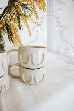 two mugs sitting on top of a table next to a vase with yellow flowers