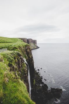 a waterfall is coming out of the side of a cliff into the ocean on a cloudy day