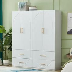 a white cabinet with two doors in a green room next to a bed and potted plant