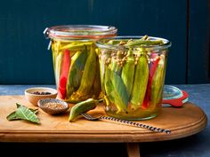 two jars filled with pickled vegetables on top of a wooden cutting board next to a spoon