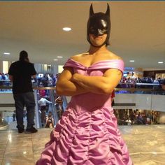 a woman in a pink dress is standing with her arms crossed and wearing a batman mask