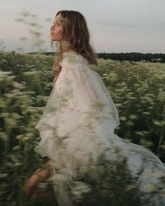 a woman in a white dress walking through a field