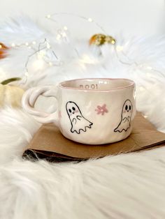 a cup with two ghost faces painted on it sitting on top of a brown envelope