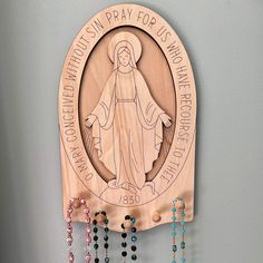 a wooden plaque with beads hanging from it's sides, depicting the virgin mary