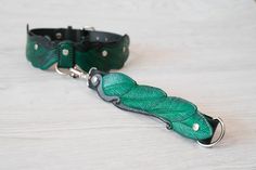 a green leather collar with leaves attached to it on a white table next to a black leash