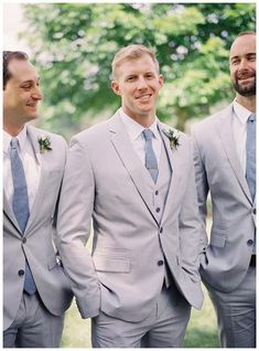 three men in grey suits and ties standing next to each other with trees in the background