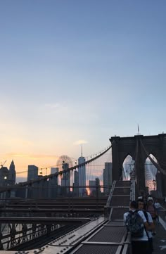 people walking across the brooklyn bridge at sunset