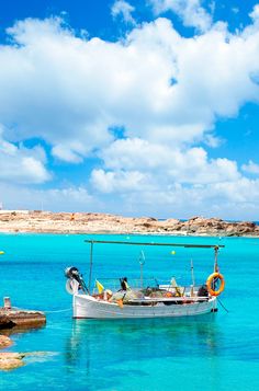 a small boat floating on top of a body of water next to a sandy beach