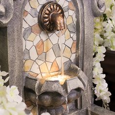 a fountain with water pouring out of it's sides and white flowers in the background