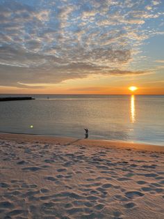 the sun is setting over the ocean and people are walking on the beach