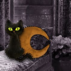 a black cat sitting on top of a couch next to a yellow crescent moon and potted plant